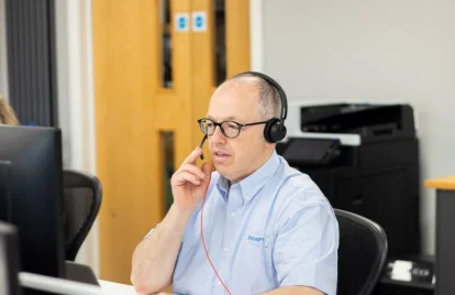 man die een laptop gebruikt terwijl hij via een headset een telefoongesprek voert